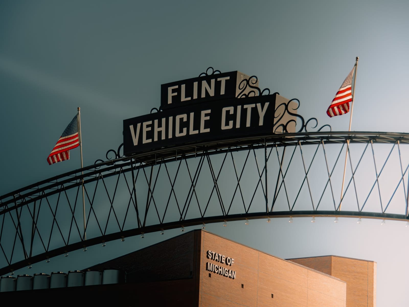 The Flint Vehicle City arch over Saginaw Street, with American flags on each end and a storm-gray sky