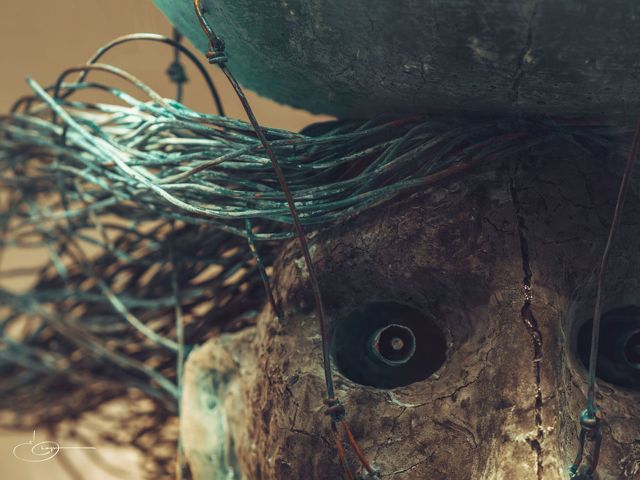 Close-up of a cracked doll face with one dark eye, tangled in loose wire