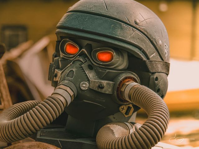 A figure in a helmet and gas mask with glowing red eyes and ribbed breathing hoses