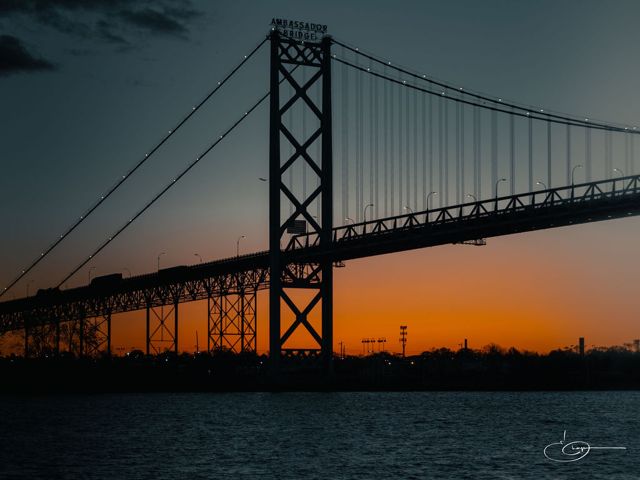 A suspension bridge silhouetted against an orange sunset over the water