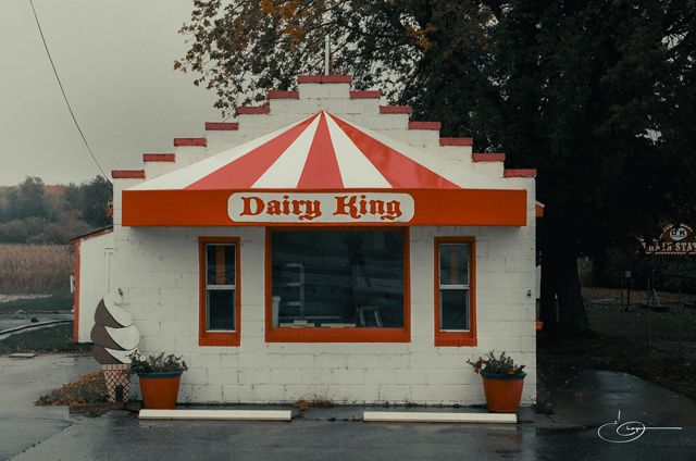 A small white ice cream stand with a red and white striped roof and a Dairy King sign, on a gray day